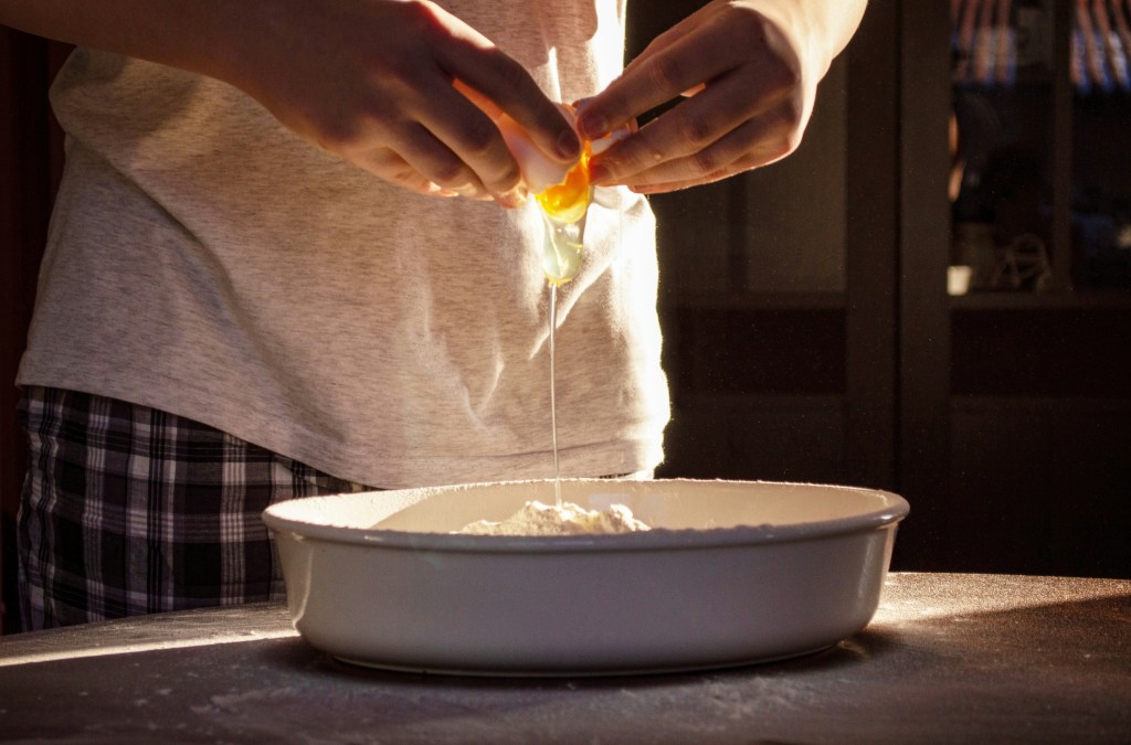 hand holding a cracked egg over a bowl of flour